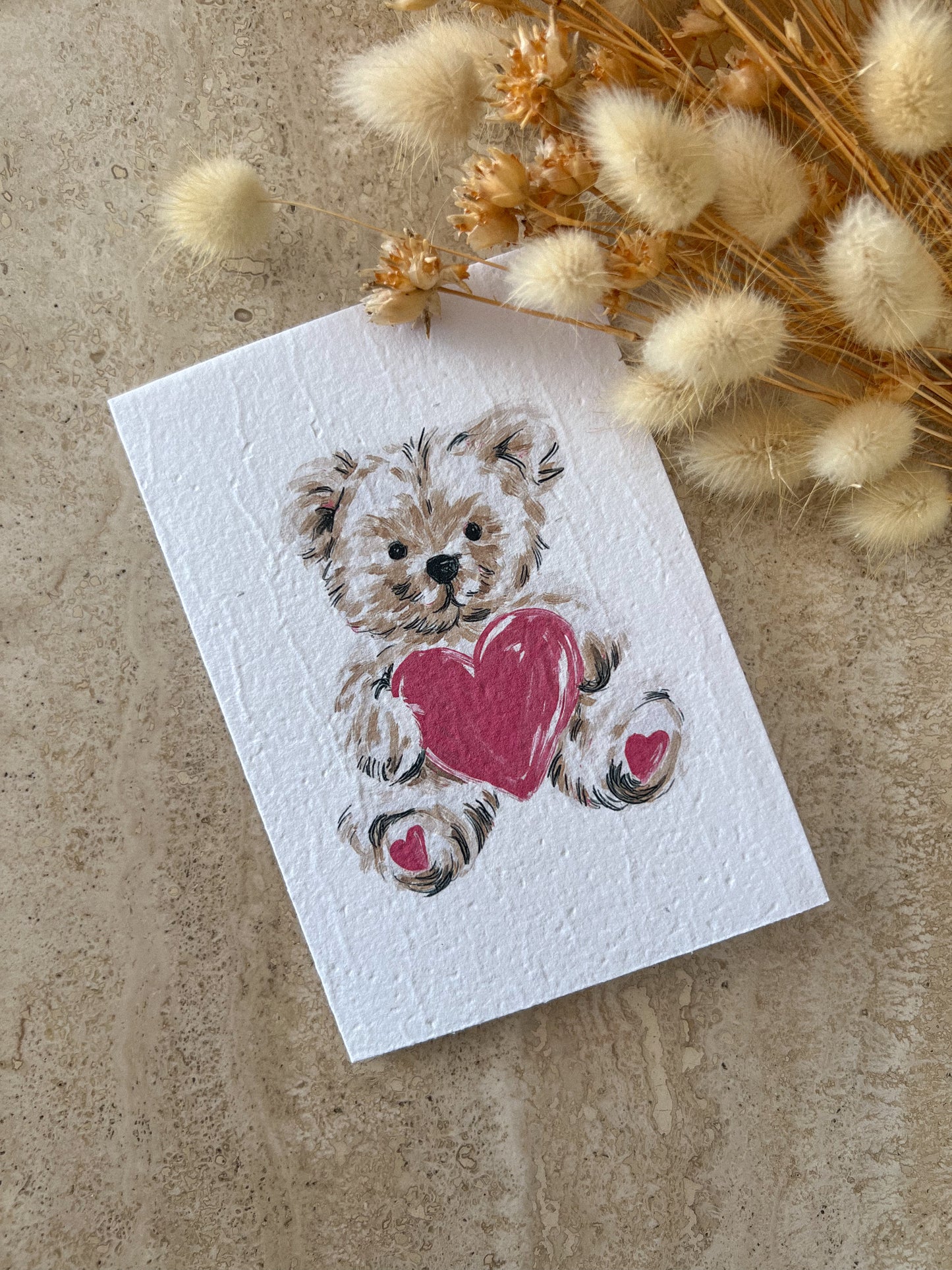 Plantable greeting card with a teddy bear holding a heart on a textured surface with dried flowers by Willow & Sage Co.