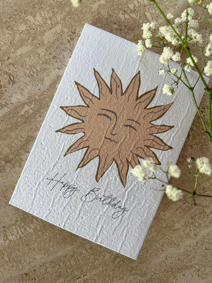 White plantable greeting card with sun design and 'Happy Birthday' text on a textured surface with flowers. Card by Willow & Sage Co.