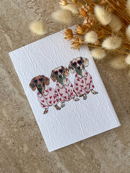 Card with illustration of three dogs in pajamas on a textured surface with dried flowers, by Willow & Sage Co.