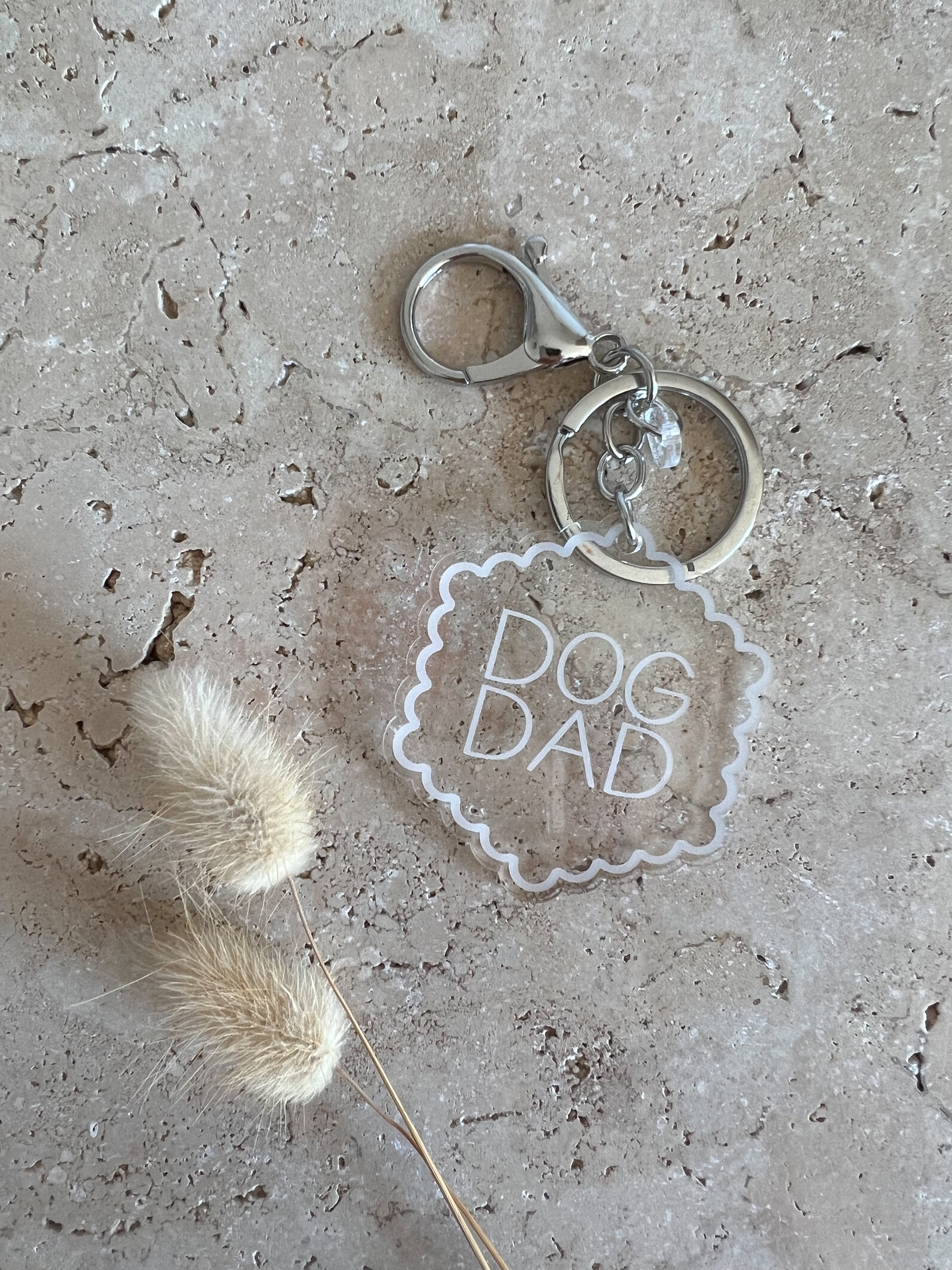 Keychain with 'Dog Dad' tag on a textured surface with dried grass