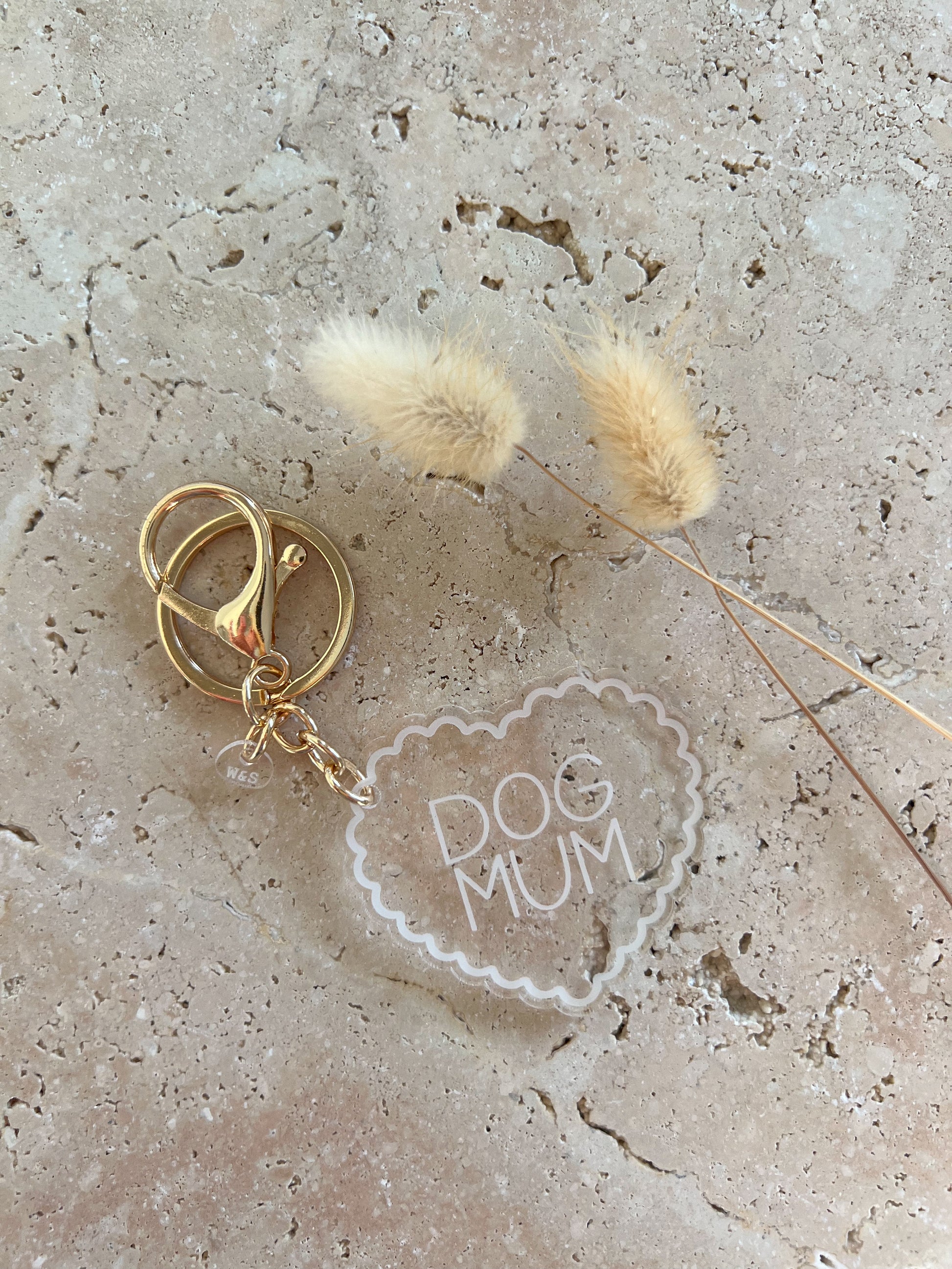 Gold keychain with 'DOG MUM' charm on a textured surface with dried flowers.