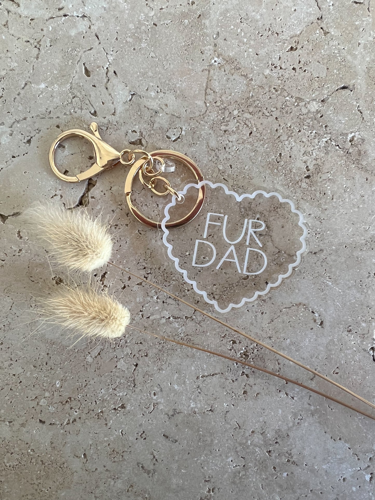 Keychain with 'Fur Dad' tag and dried flowers on a concrete surface