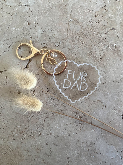 Keychain with 'Fur Dad' tag and dried flowers on a concrete surface