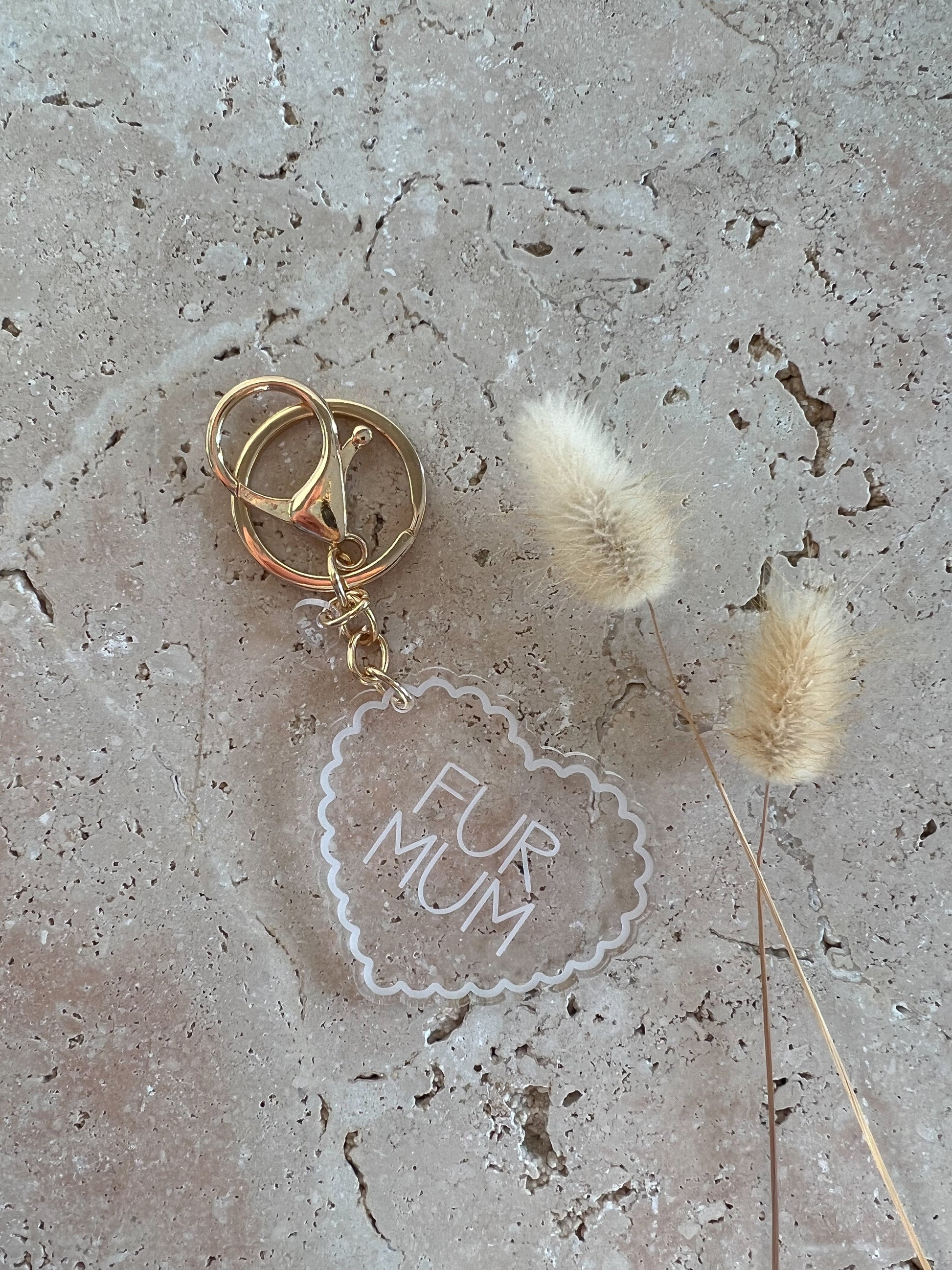 Gold keychain with 'Fur Mum' tag on a textured surface with dried grasses.