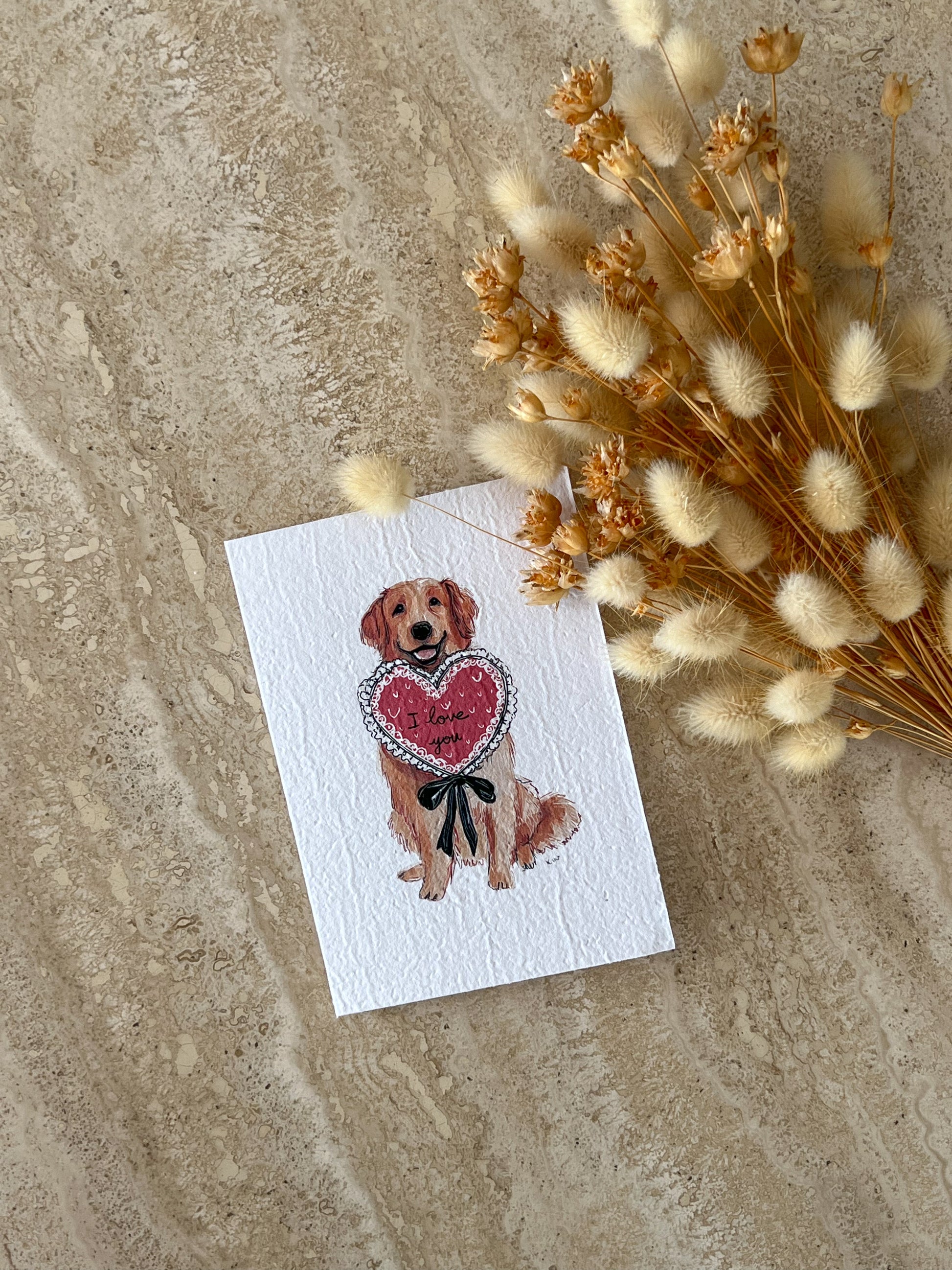 Card with a Golden Retriever dog holding a heart and flowers on a textured surface by Willow & Sage Co.