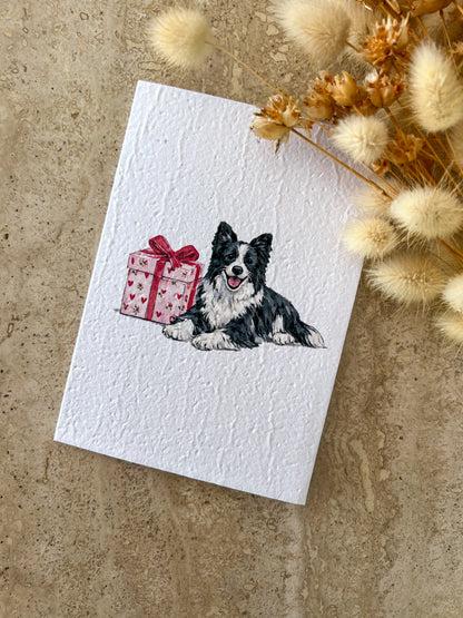 Card with a Border Collie dog illustration and gift box on a textured surface with dried flowers, by Willow & Sage Co.