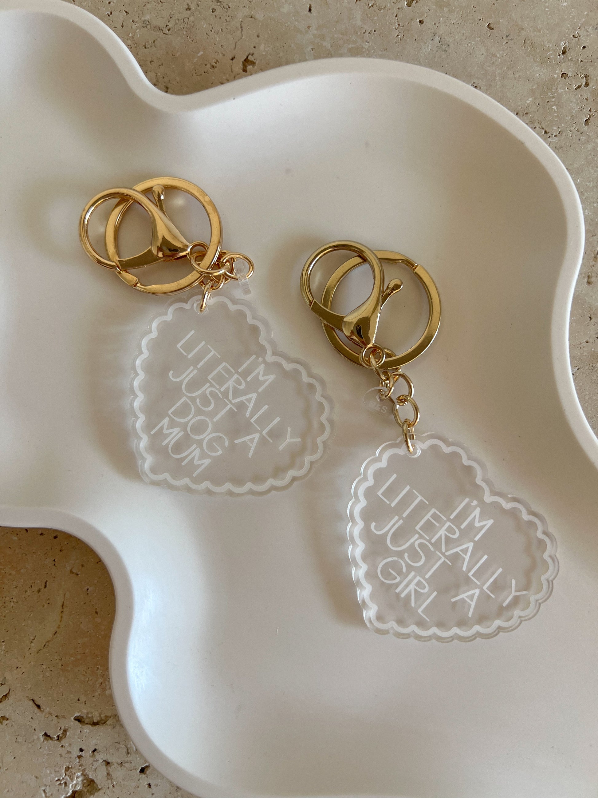 Two gold keychains by Willow & Sage Co with engraved text on a white dish.