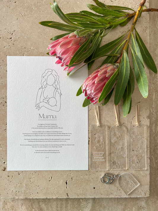 A gift set for breastfeeding mothers including a print, a bookmark, and a keychain, displayed on a stone surface with pink flowers.