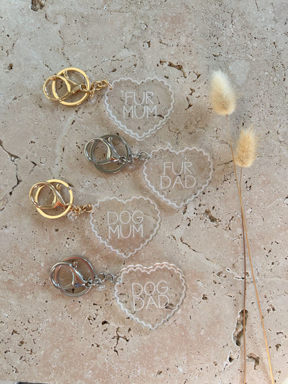 Heart-shaped keychains with 'Fur Mum', 'Fur Dad', 'Dog Mum', and 'Dog Dad' text on a textured surface.