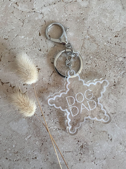 Star-shaped keychain with 'DOG DAD' text on a textured surface with dried pampas grass.