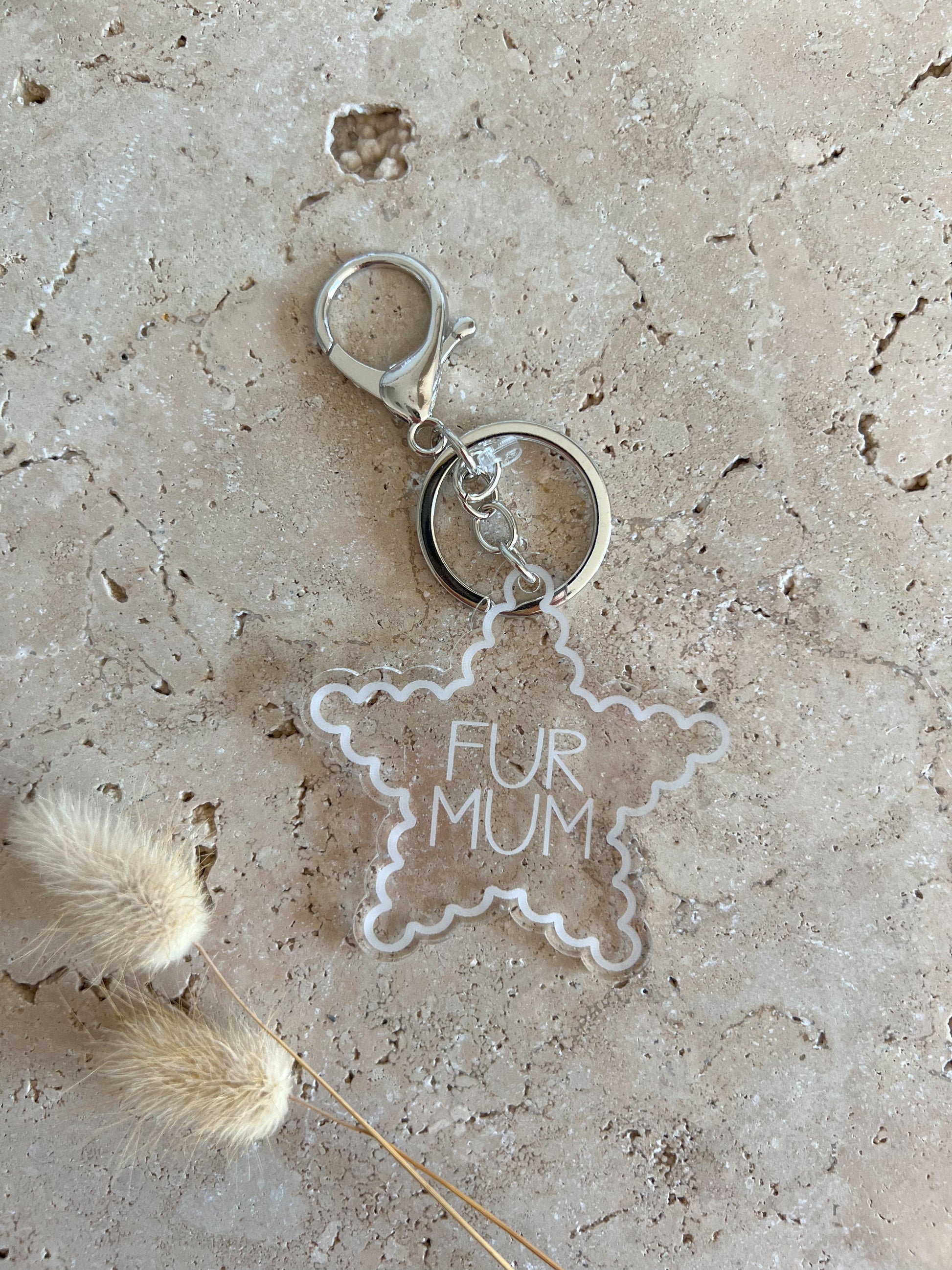 Star-shaped keychain with 'FUR MUM' text on a textured surface with dried plants.