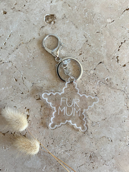 Star-shaped keychain with 'FUR MUM' text on a textured surface with dried plants.