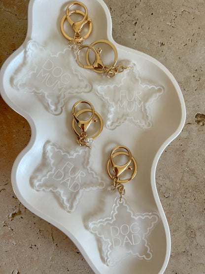 Gold dog keychains on a white dish with engraved text on a beige surface