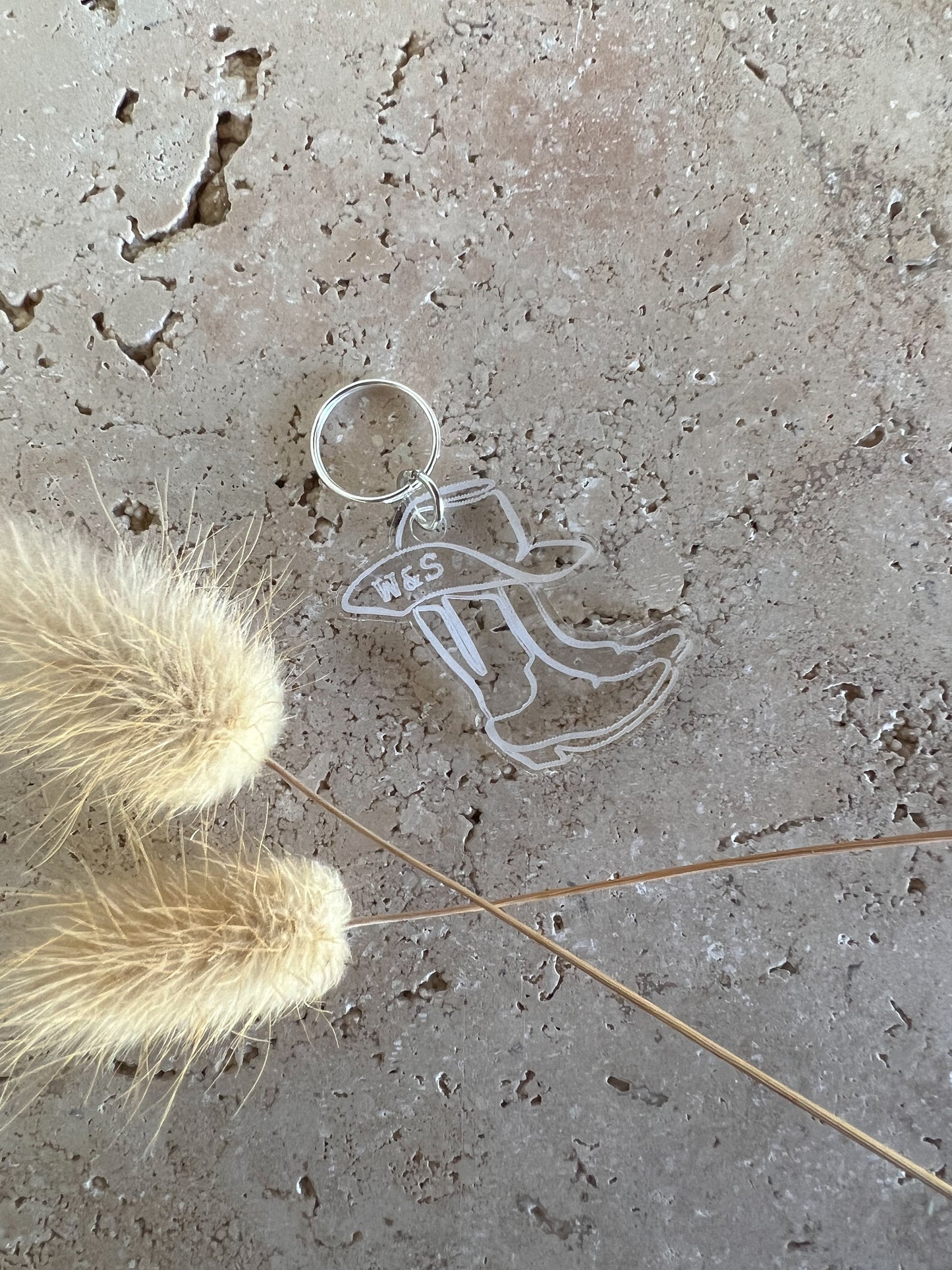 Clear cowboy boot pet tag on a textured surface with dried grasses.